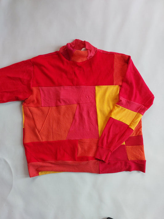 Front view of the upcycled orange merino wool turtleneck flat lay showing geometric colour-block panels.