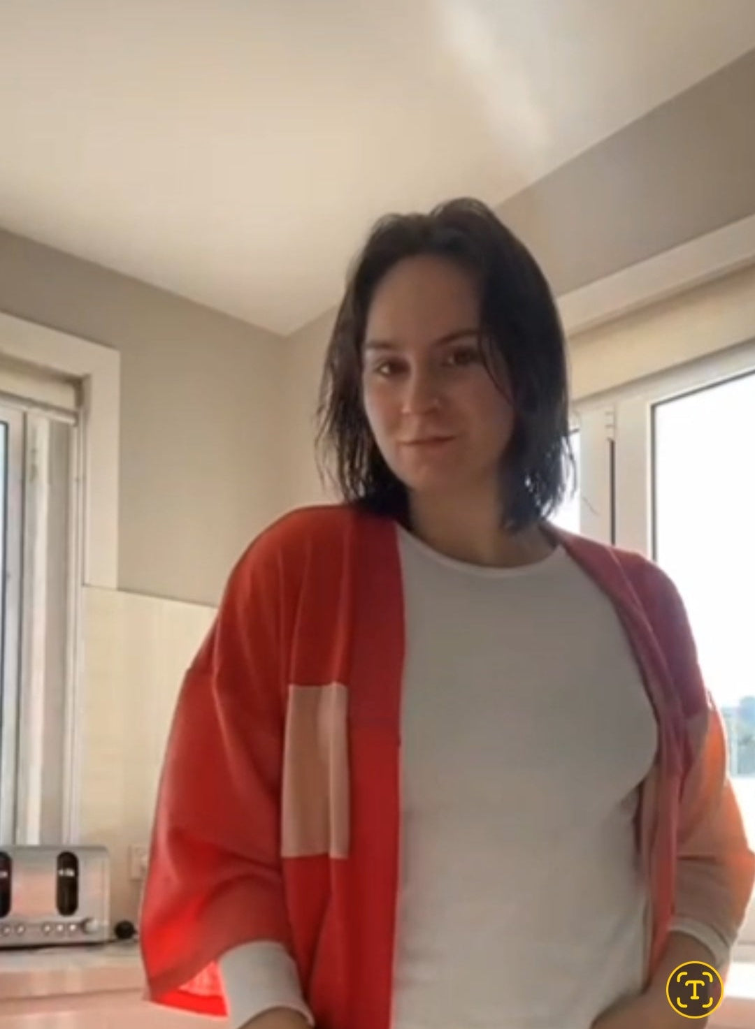 Person wearing a red cardigan over a white shirt in a kitchen setting
