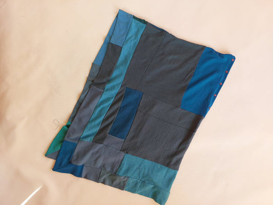 Flat lay view of a similar, longer style upcycled merino wool poncho in a multi tonal teal, aqua blue, and green patchwork combination.