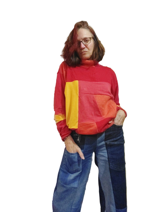 Model wearing a vibrant orange, yellow, and red patchwork upcycled merino wool turtleneck sweater with denim jeans.