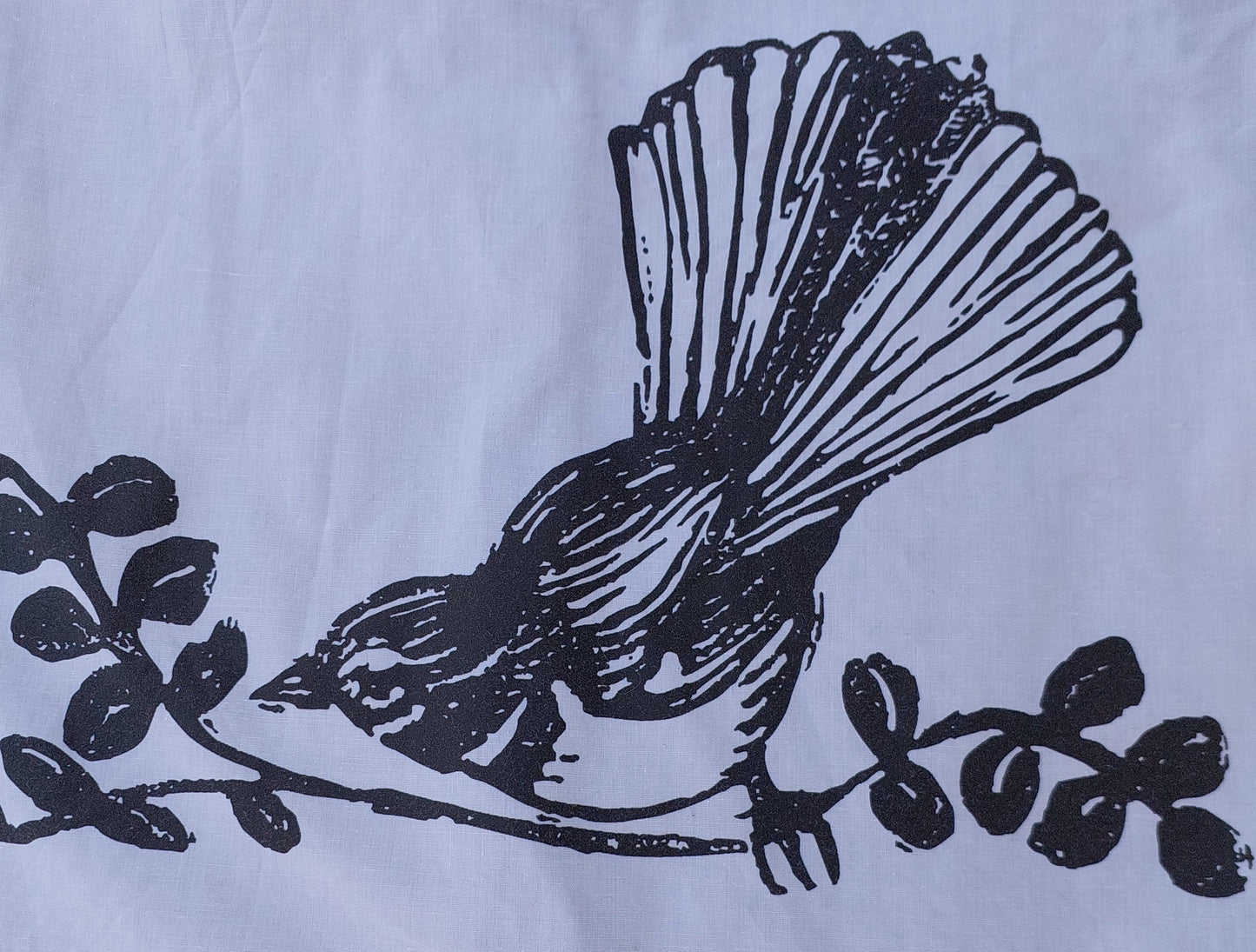 Detailed view of the hand-screenprinted piwakawaka (fantail) bird design on reclaimed textile, showcasing the artisanal texture.