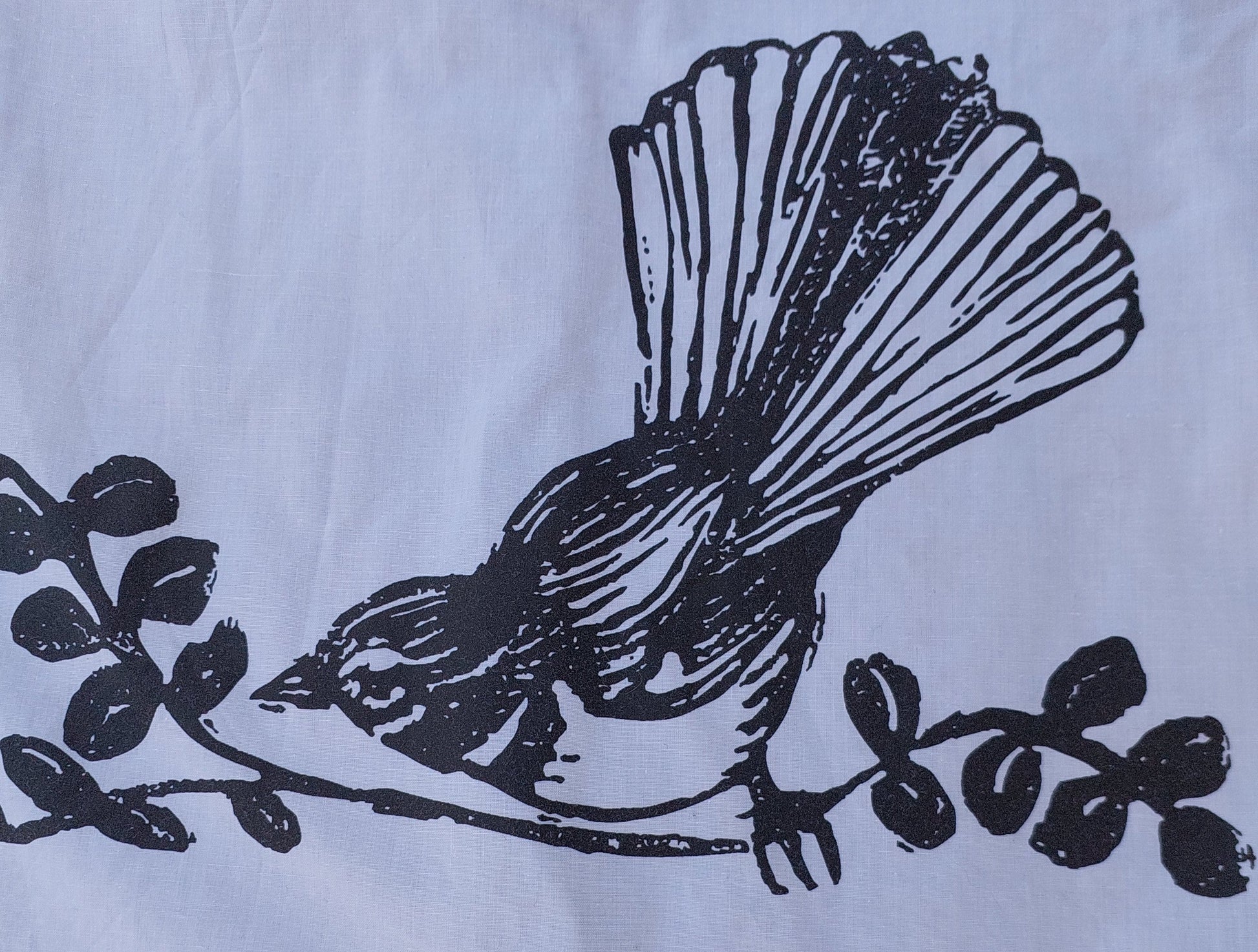Detailed view of the hand-screenprinted piwakawaka (fantail) bird design on reclaimed textile, showcasing the artisanal texture.